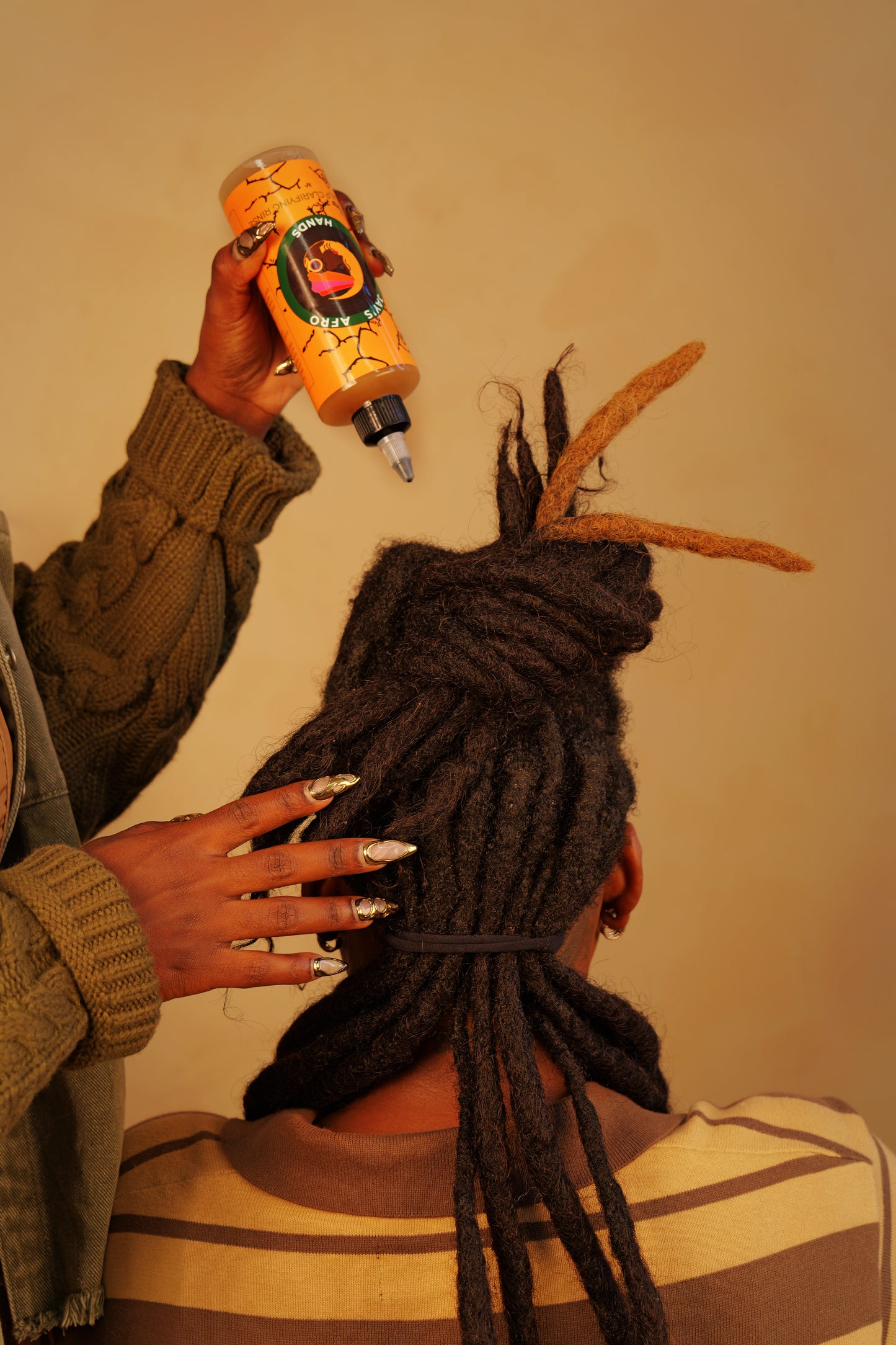 Person with dreadlocks holding a bottle of hair product against a plain background
